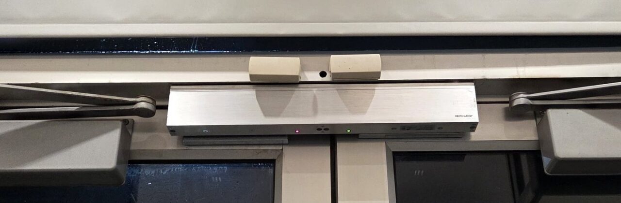 Automatic door operator mounted on the header over commercial double glass doors, Bronx, NYC