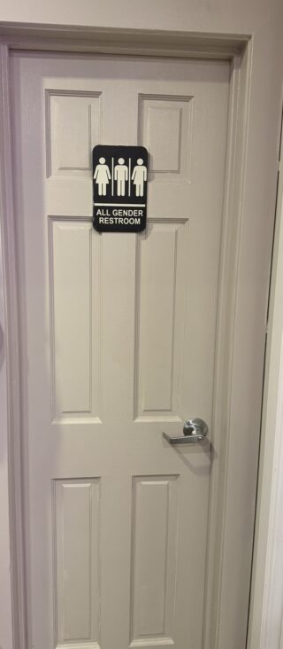 White six-panel interior bathroom door with a satin-finish lever privacy lock and an all-gender restroom sign, installed by Metro Local Locksmith on the Upper East Side, Manhattan