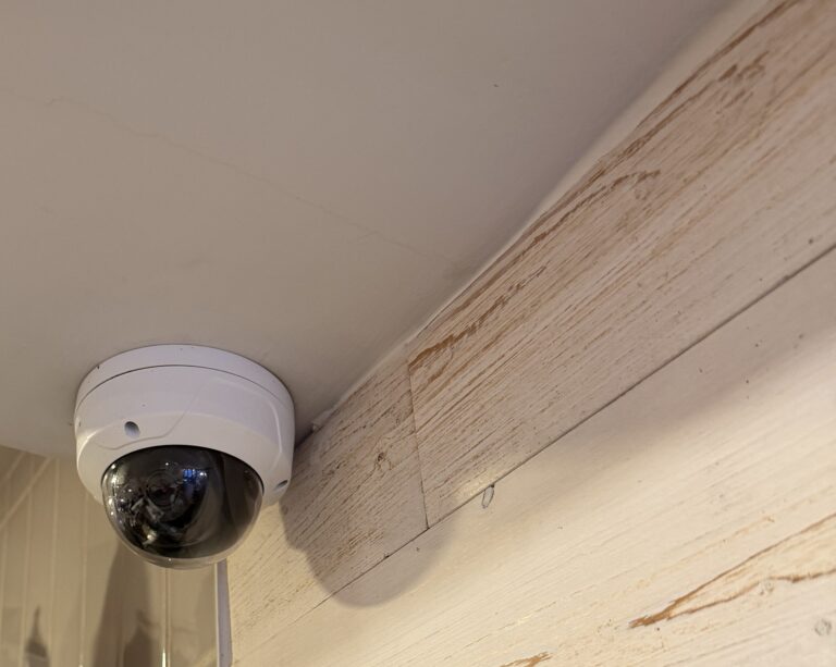 White dome security camera mounted at the ceiling beside a whitewashed wood wall, installed by Metro Local Locksmith on the Upper East Side, Manhattan