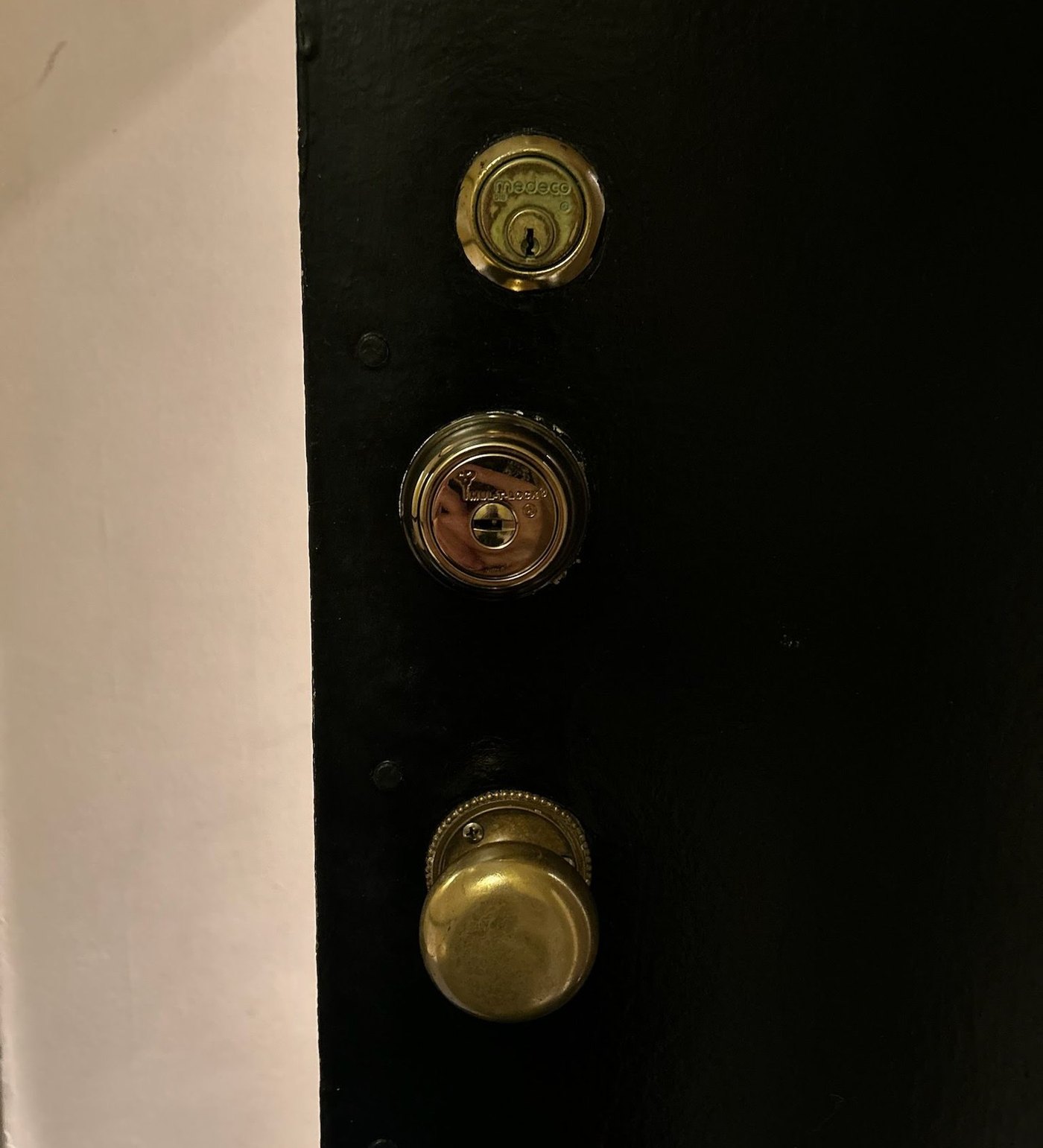 Brass lock cylinders and a knob on a black door, lock work by Metro Local Locksmith, NYC