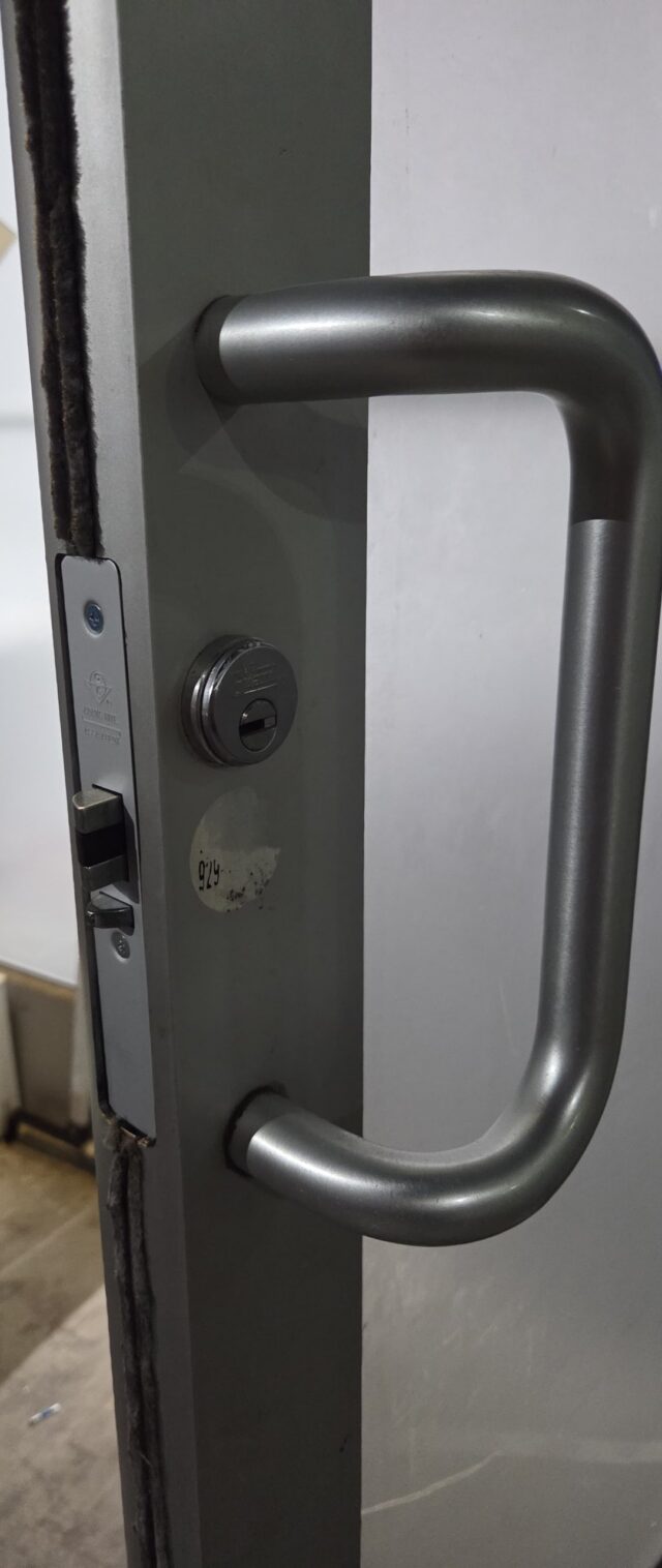 Offset pull handle with keyed cylinder on a dark aluminum commercial storefront door, Bronx, NYC