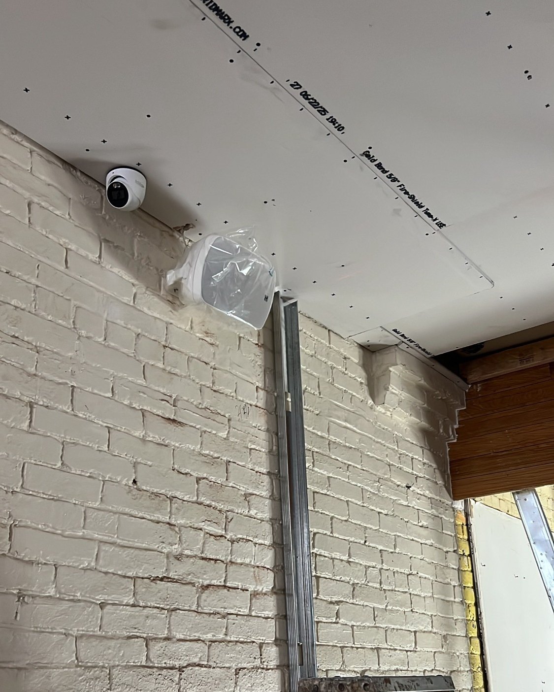 Security camera install on brick wall - Metro Local Locksmith Security camera and conduit being installed on a white brick wall, Metro Local Locksmith