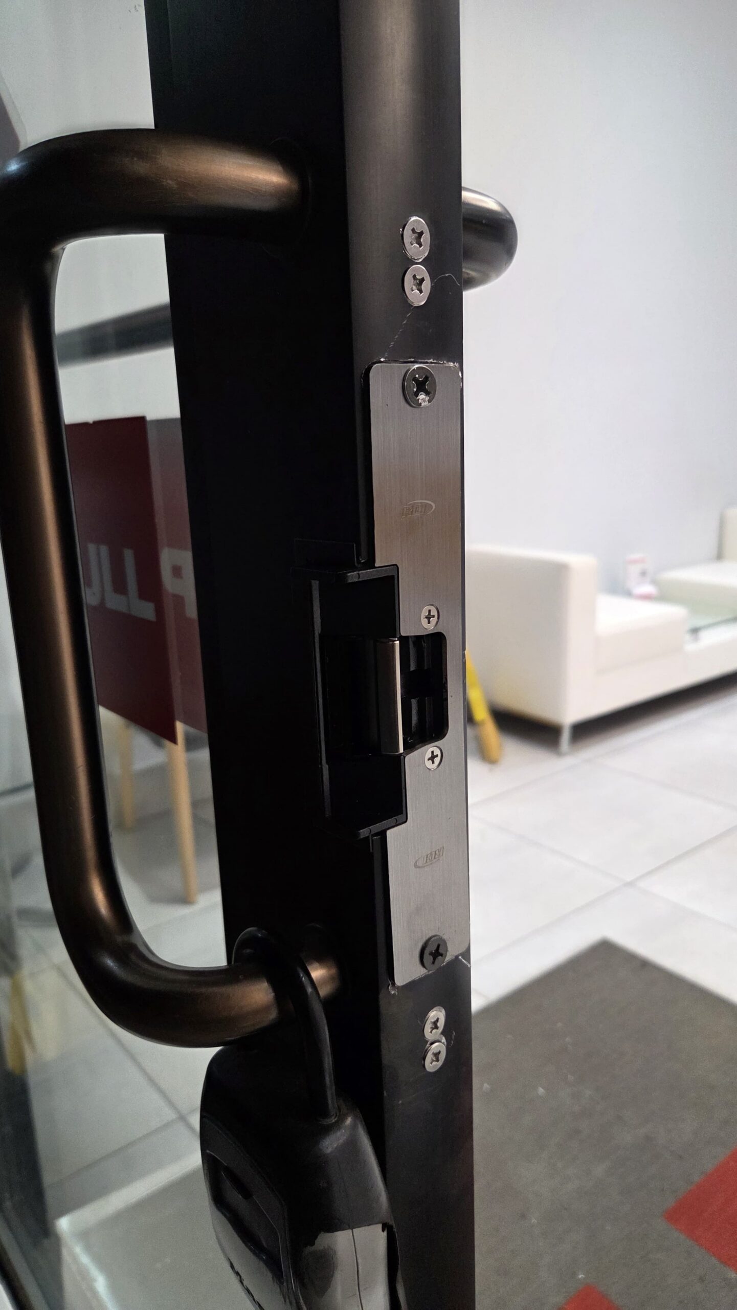 Electric strike installed in the frame of a commercial aluminum glass door beside the pull handle, Bronx, NYC